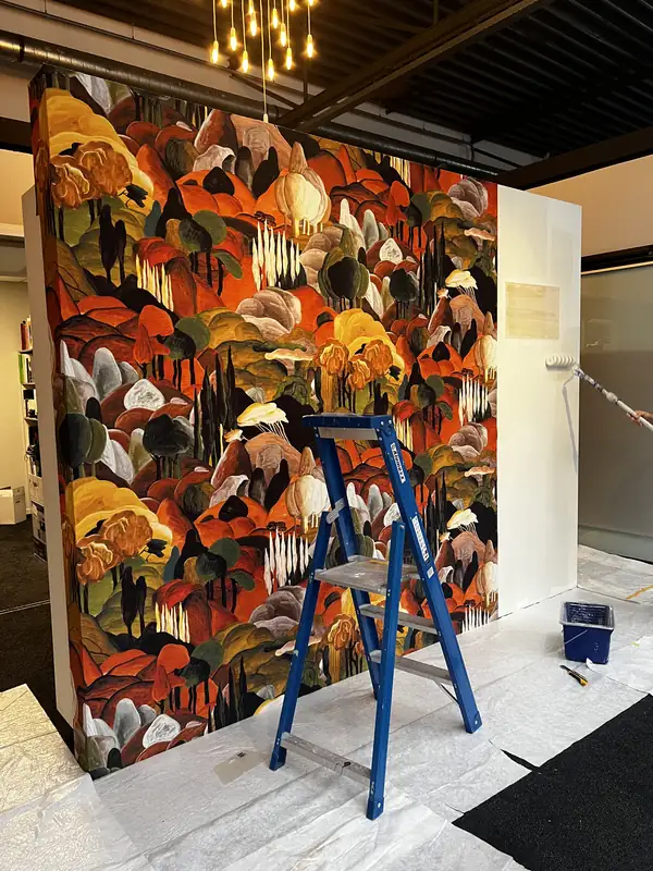 Een wandvullend dessin met een kleurrijk landschap wordt aangebracht, met een trap voor de wand