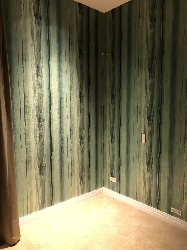 Hoek van een kamer met groen behang met onregelmatige verticale strepen