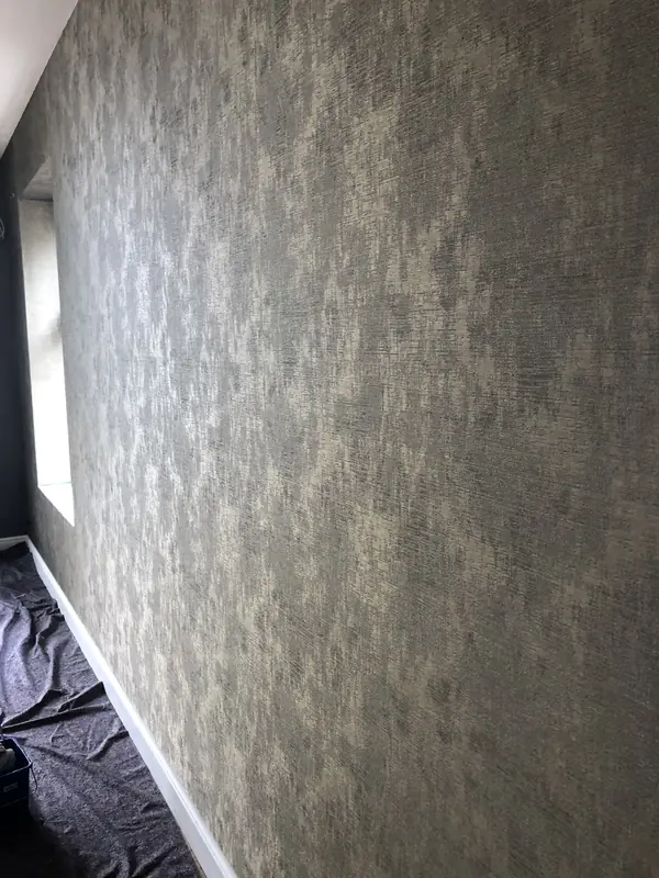 Lange wand met grijsgroen structuurbehang met goud, de vloer is afgedekt met stucloper